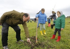 Una familia planta un ejemplar de arbolado autóctono en el barrio de Lloreda, en Tremañes, para reforestar un bosque con 300 ejemplares.