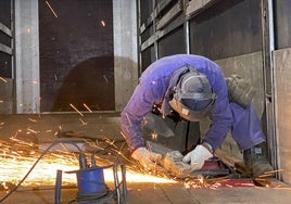 Un trabajador repara la plataforma de un camión en un taller asturiano.