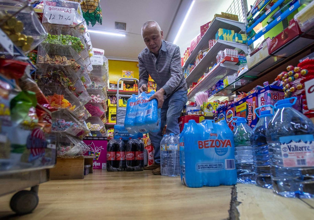 Aixiong Ye reponiendo botellas y garrafas de agua en su tienda.