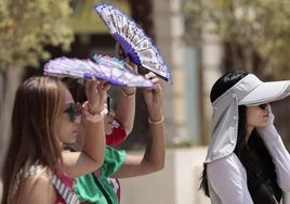 Unas turistas se protegen del sol y del calor con abanicos y gorras.